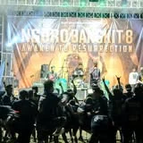 Band tampil di depan backdrop NGORO BANGKIT 8 Awaken to Resurrection dengan penonton di depan panggung